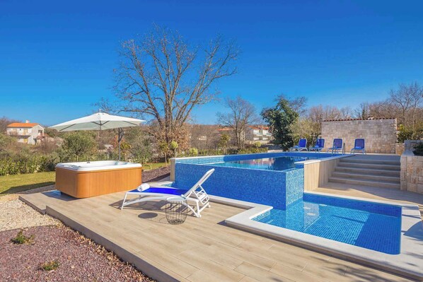 A swimming pool with blue tiles, a hot tub, and lounge chairs.