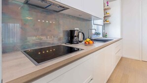 Una cocina moderna con gabinetes blancos, una placa de inducción negra y una campana extractora de acero inoxidable.