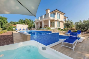 Une maison moderne dotée d’une piscine, de chaises longues et d’un jacuzzi.
