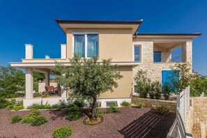Une maison à deux étages avec un balcon, une façade en pierre et un petit jardin avec un arbre.