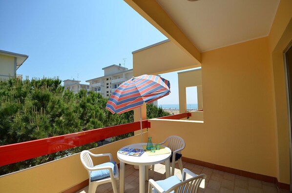 A balcony with a table, chairs, and a striped umbrella.