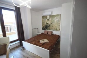 Ein Schlafzimmer mit einem Bett, einem Fenster, einem Sessel und einem Bild an der Wand.