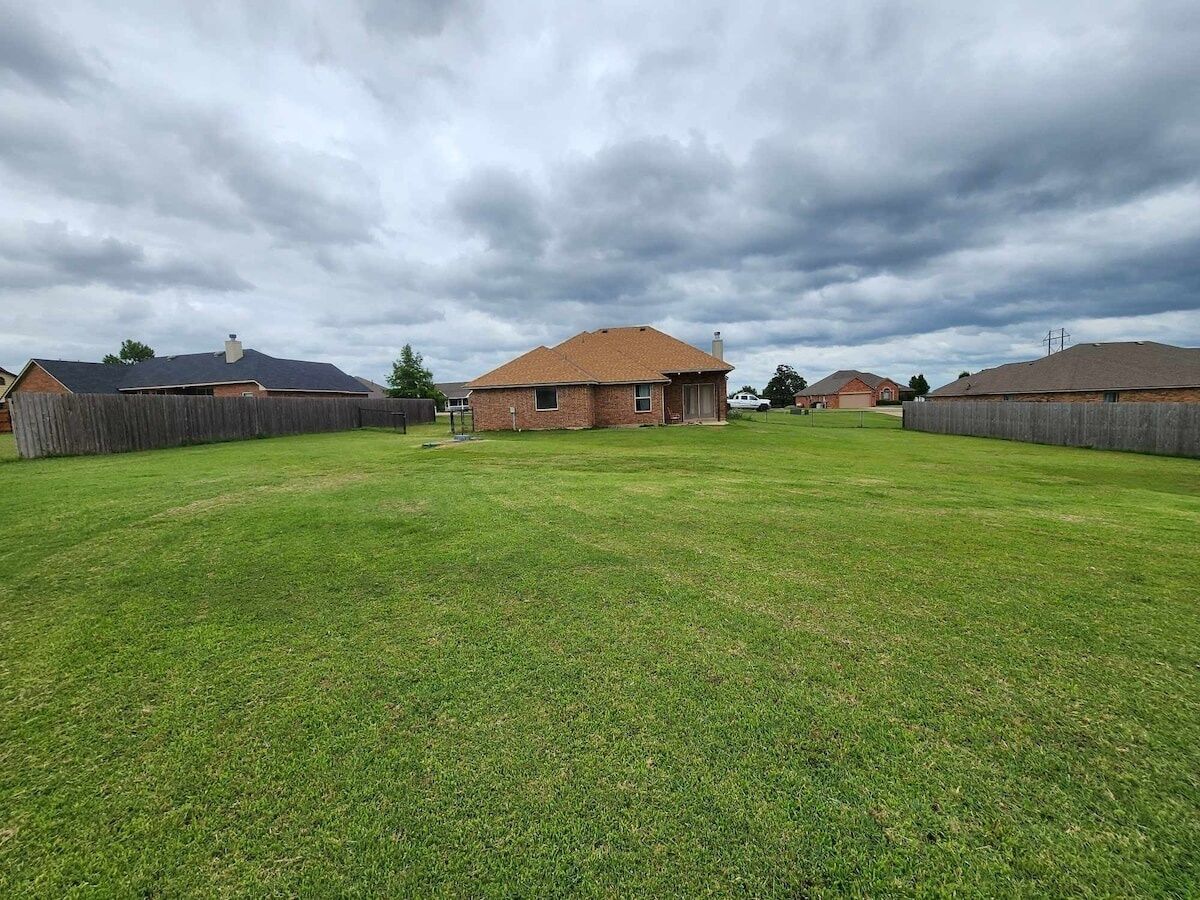 A residential area with a large grassy yard, a brick house, and a wooden fence.