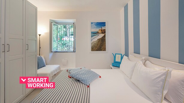 A bedroom with a bed, a desk, and a window with a view of a beach. - Comfy and Quiet in Camogli by Wonderful Italy (Camogli)