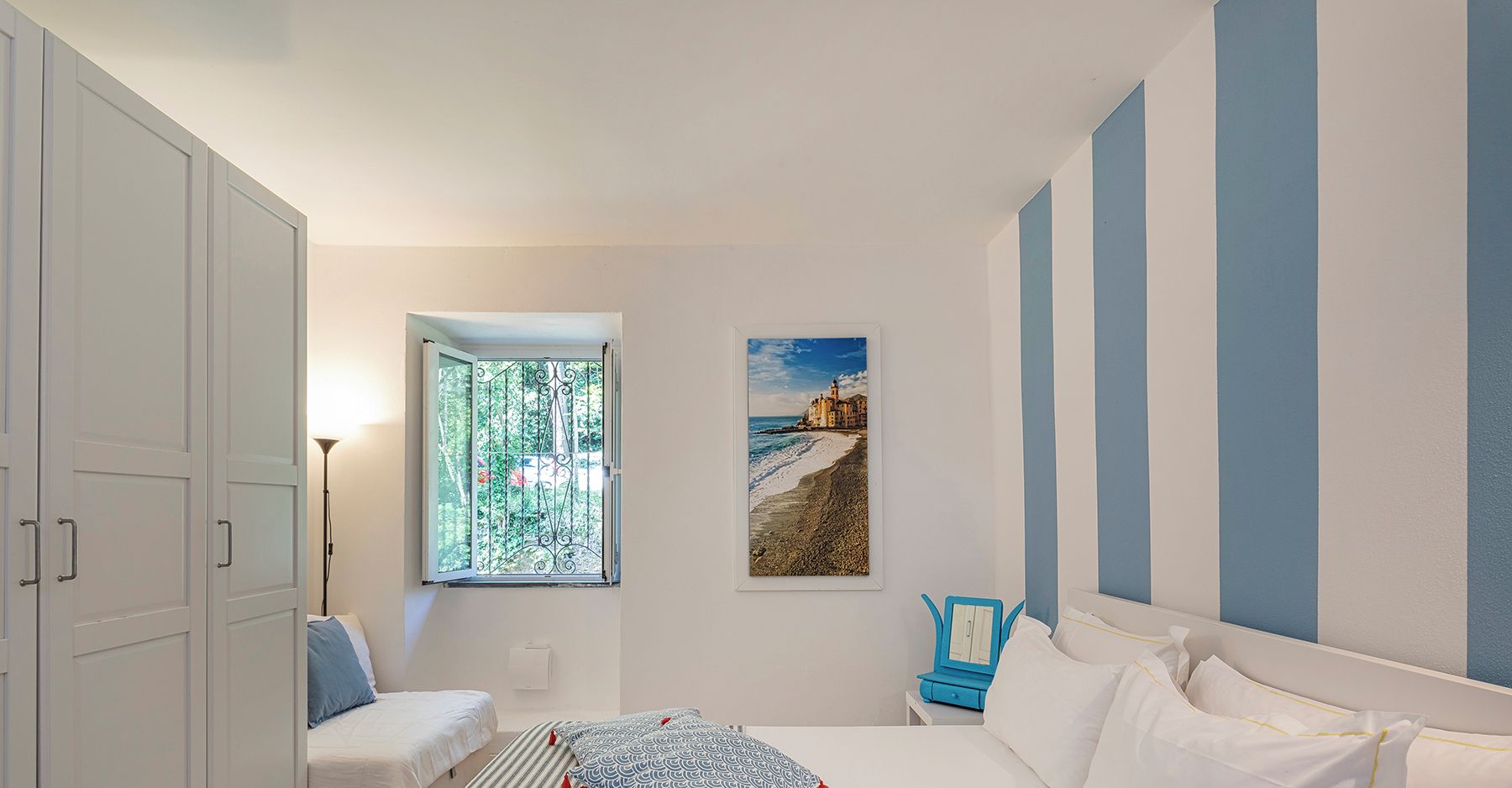 A bedroom with a bed, a desk, and a window with a view of a beach.