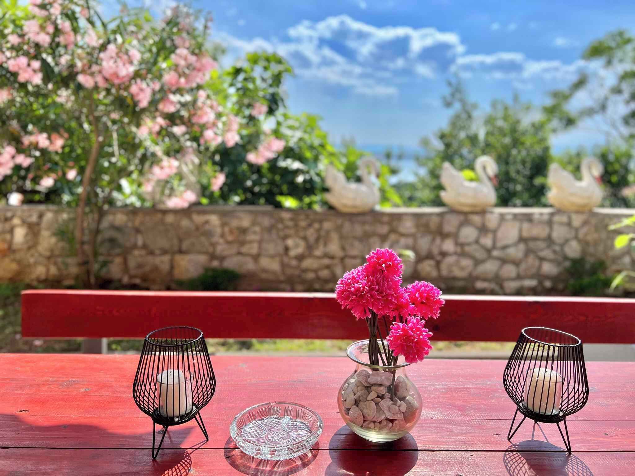 Uma mesa de madeira vermelha com dois castiçais pretos e um vaso de vidro com flores cor-de-rosa.