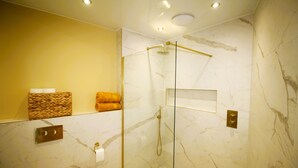 A modern bathroom with a glass-enclosed shower, marble walls, and a yellow accent wall.