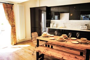 Un coin repas avec une table en bois dressée pour quatre personnes, des meubles noirs et un mur recouvert de carreaux blancs.