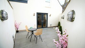 A patio with a table and chairs, a sliding glass door, and wall-mounted lights.