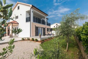 Una casa moderna de dos pisos con un balcón, camino de grava y jardín.