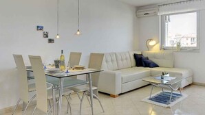 A modern living room with a glass dining table, white sofa, and a glass coffee table.