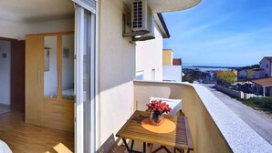 A balcony with a wooden table and a vase of flowers, a sliding glass door, and a view of a residential street.