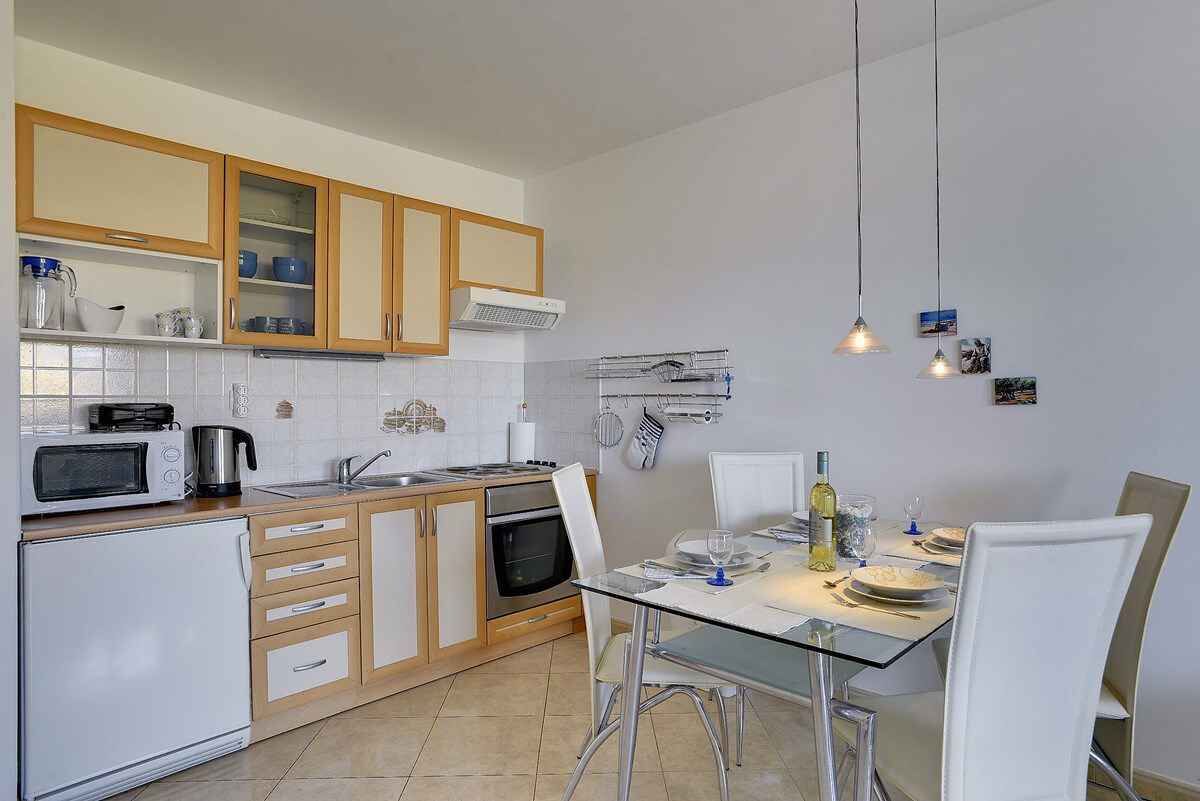 A modern kitchen with wooden cabinets, a microwave, a kettle, and a dining area with a glass table and chairs.