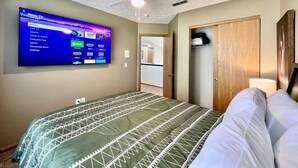 Un dormitorio con cama, ventilador de techo, televisor montado en la pared mostrando la interfaz de Roku TV y un armario de madera.