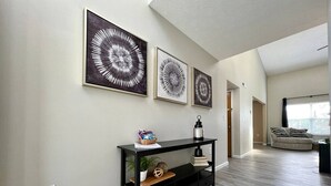 Una sala de estar con una consola negra, tres obras de arte enmarcadas, un sofá y una ventana con persianas.