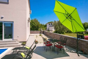 Eine Terrasse mit Pool, Sitzgelegenheiten im Freien und einem leuchtend grünen Sonnenschirm.