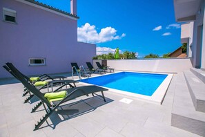 Relax by the rectangular pool surrounded by sun loungers and a light-colored wall.