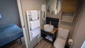 Un baño de hotel pequeño con lavamanos, inodoro, perchero para toallas y espejo.