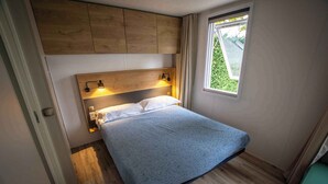 Un dormitorio pequeño con cama, cabecera de madera, lámparas de noche y ventana con vistas.