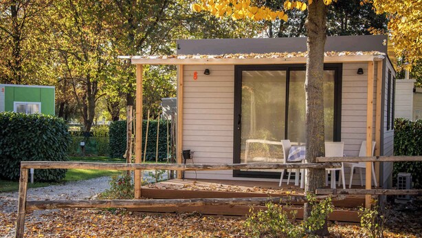 Una casa pequeña de un piso con porche cubierto, puerta corrediza de vidrio y un pequeño espacio exterior con mobiliario.