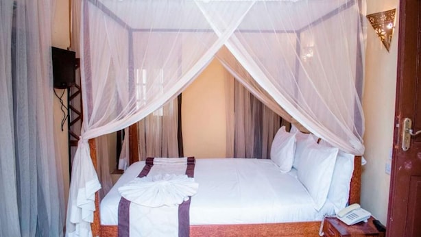 A bed with a canopy, a bedside table with a phone, and a wall-mounted light fixture. - Island Stone Town Hotel (Zanzibar Town)
