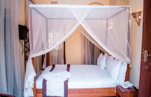 A bed with a canopy, a bedside telephone, and a wall-mounted light fixture. - Island Stone Town Hotel (Zanzibar Town)