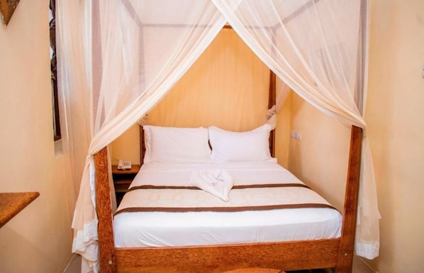 A bed with a canopy, white bedding, and a wooden headboard. - Island Stone Town Hotel (Zanzibar Town)