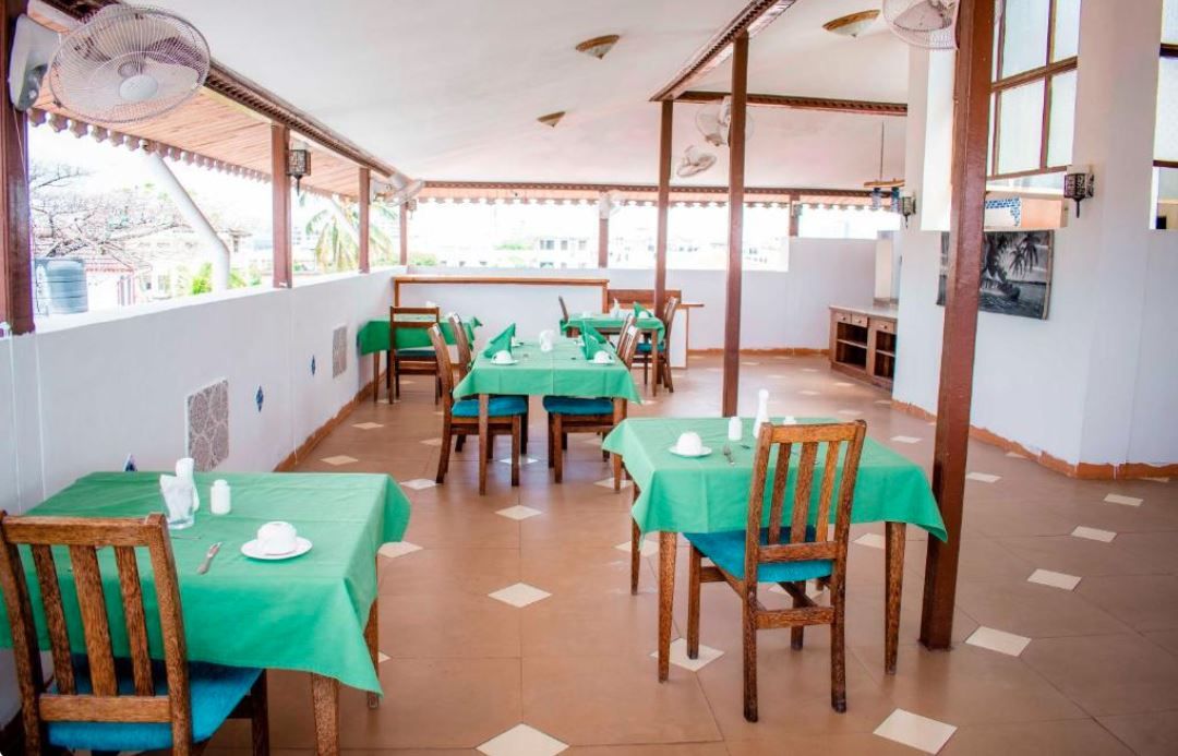 Un restaurant dont les tables sont recouvertes de nappes vertes, avec des chaises en bois et un sol carrelé.