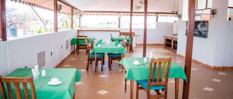 Un restaurant dont les tables sont recouvertes de nappes vertes, avec des chaises en bois et un sol carrelé.