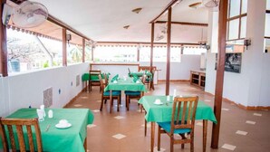 A restaurant with tables covered in green tablecloths, wooden chairs, and a tiled floor. - Island Stone Town Hotel (Zanzibar Town)