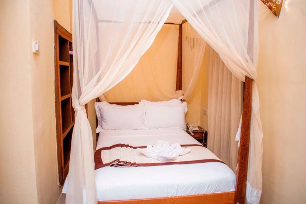 A bed with a canopy, white bedding, and a folded towel on the bed.