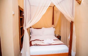 A bed with a canopy, white bedding, and a folded towel on the bed. - Island Stone Town Hotel (Zanzibar Town)