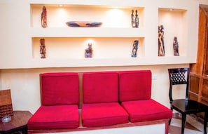 A red sofa in a room with shelves above displaying various sculptures. - Island Stone Town Hotel (Zanzibar Town)