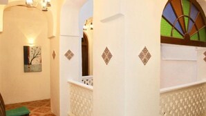 A corridor with white walls, decorative diamond patterns, a wooden bench, and a framed artwork. - Island Stone Town Hotel (Zanzibar Town)