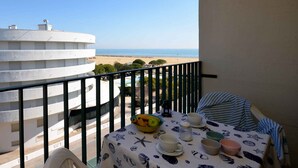 A balcony with a table set for breakfast, overlooking a beach and a white building.