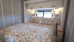 Un dormitorio con cubrecama floral, armarios blancos sobre la cama y dos lámparas fijadas a la pared.