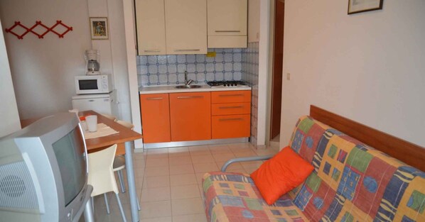 Un espacio habitable compacto con kitchenette, televisor y sofá con un cojín colorido.