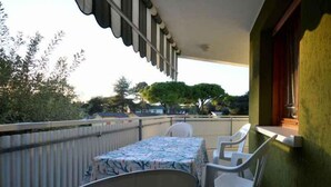 A balcony with a table and chairs, a view of trees and houses, and a green wall.