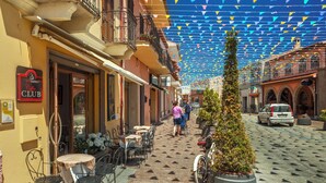 A cobblestone street with outdoor seating, a coffee shop, and a parked car. - Studio with swimming pool, near the sea (Pula Sardinien)