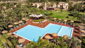 A large swimming pool with sun loungers and umbrellas, surrounded by palm trees and buildings with Mediterranean architecture. - Studio with swimming pool, near the sea (Pula Sardinien)