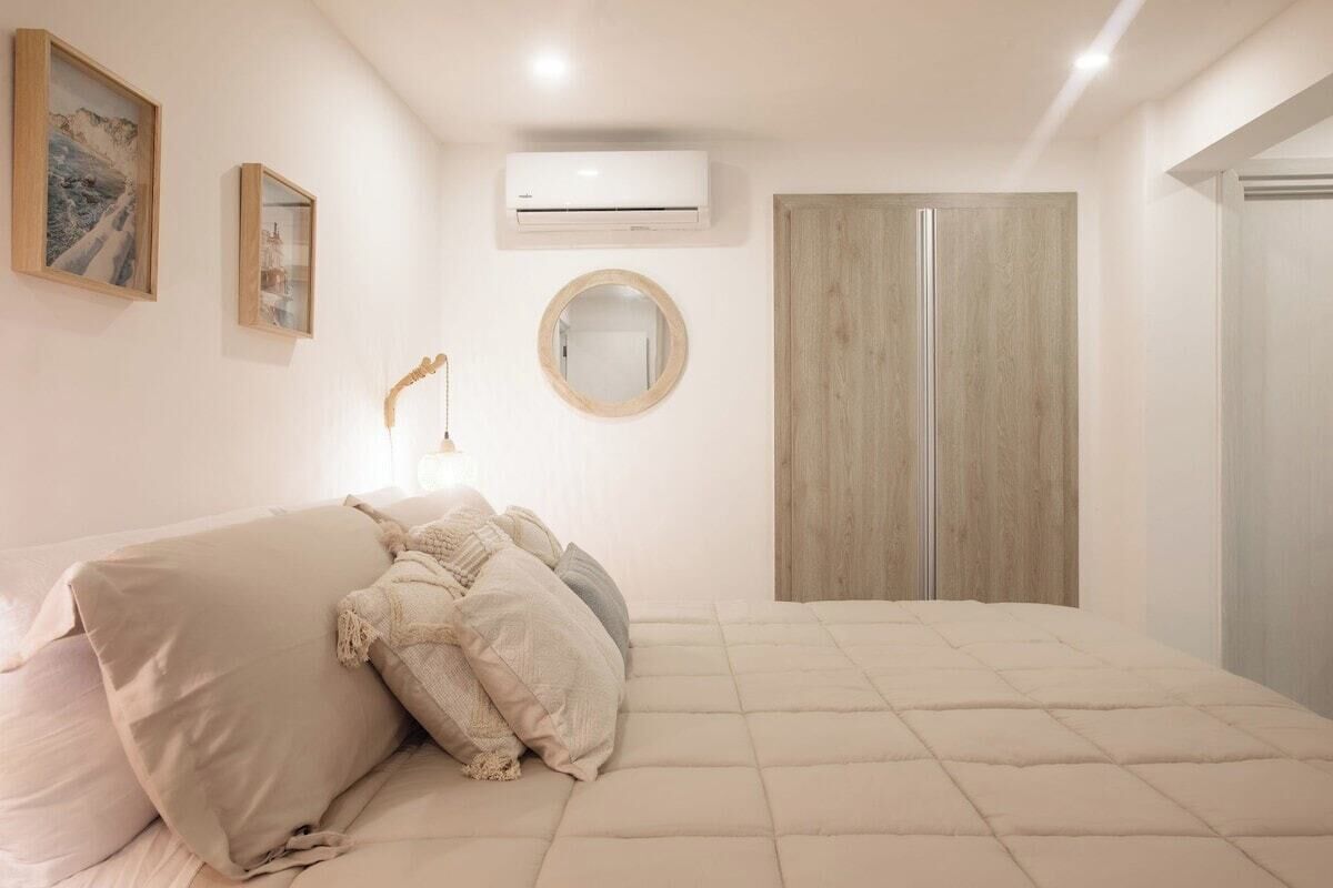 Un dormitorio con cama, armario, equipo de aire acondicionado y espejo en la pared.