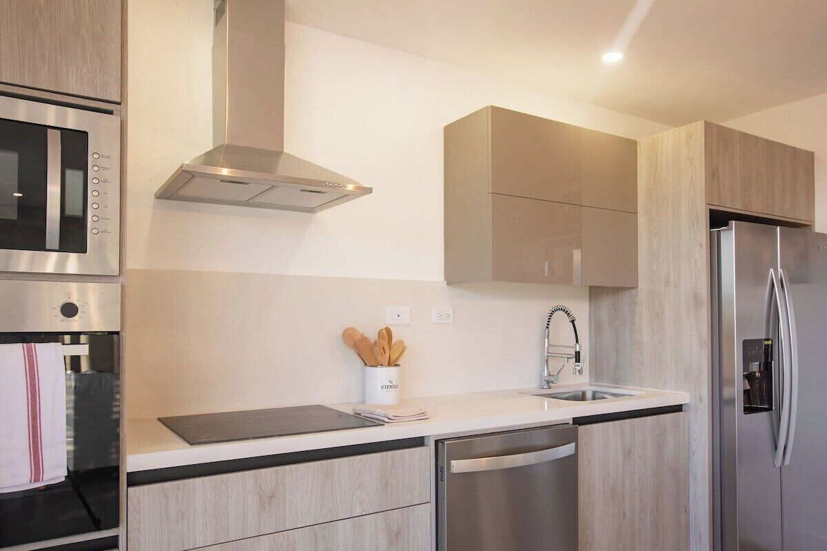 A modern kitchen with a built-in oven, microwave, stainless steel refrigerator, and a sink with a faucet.