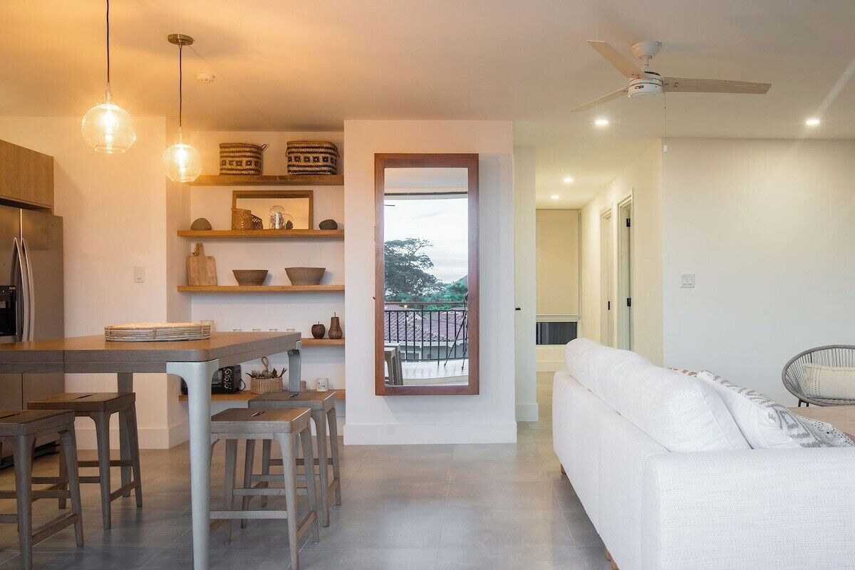 A modern kitchen with a dining area, a white sofa, and a balcony with a view.