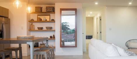 A modern kitchen with a dining area, a white sofa, and a balcony with a view.