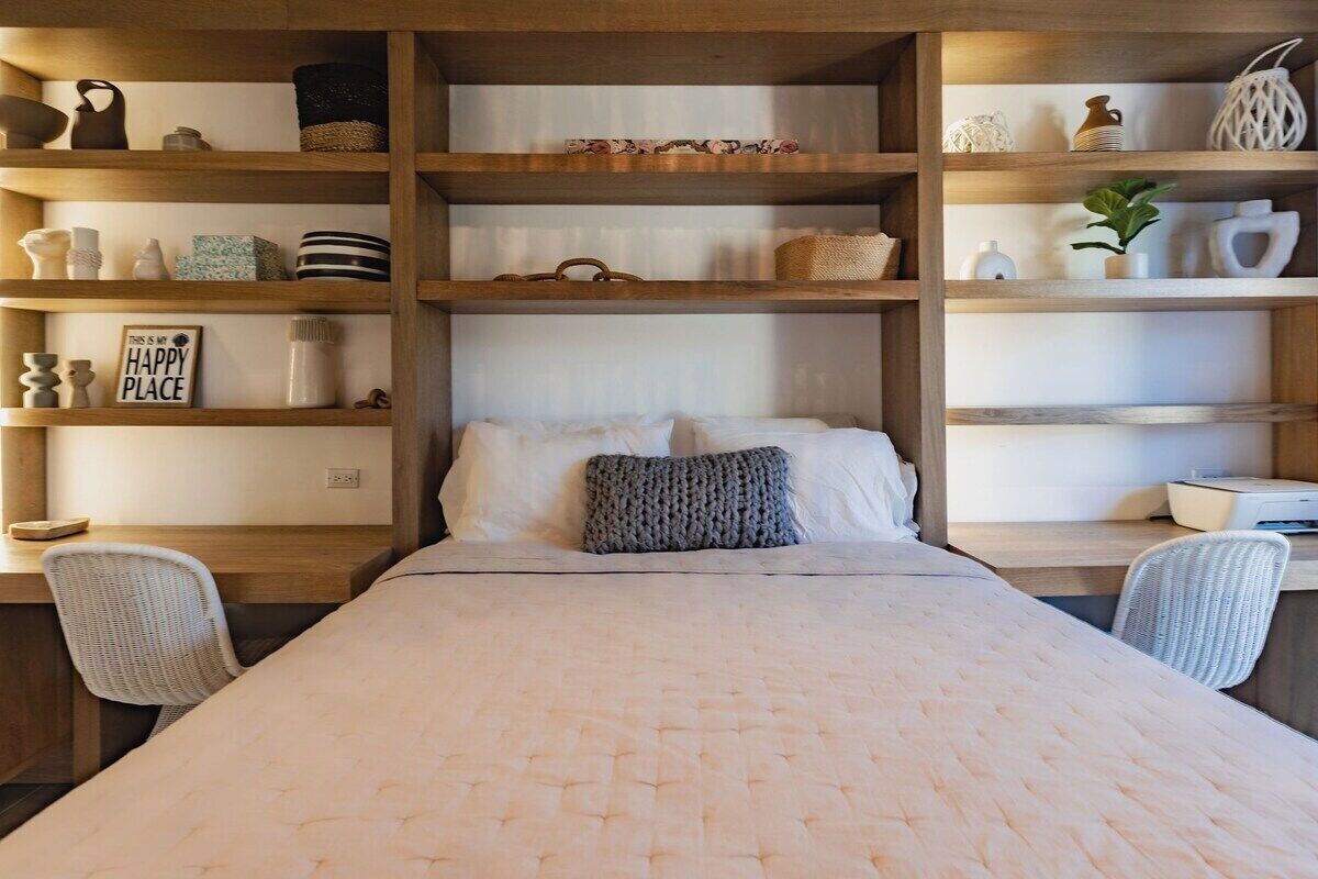 Een netjes opgeruimde slaapkamer met een bed, twee stoelen en planken met diverse decoratieve objecten.