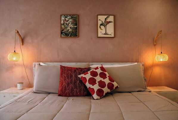 A bedroom with a bed, two wall-mounted lamps, and two framed botanical prints on the wall.