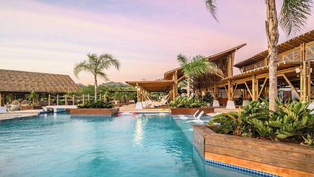 Un área de piscina con mobiliario de cubierta de madera y palmeras.