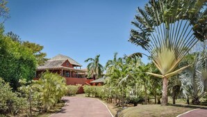 Una villa roja con techo de tejas, rodeada de exuberante vegetación tropical y un camino de entrada curvo.