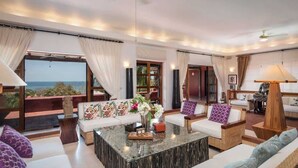 Un amplio salón con un gran ventanal que ofrece vista al océano, una mesa de centro y un conjunto de sofás y sillones.