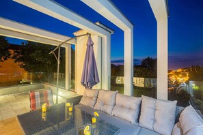 Un espace extérieur moderne, aménagé avec des sièges confortables, une table en verre et offrant une vue sur le paysage urbain au crépuscule.